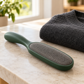 Handheld garment lint brush beside folded clothing